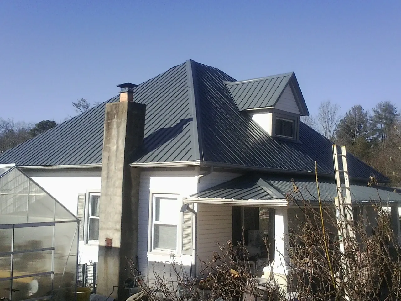 Dark blue standing seam metal roof on a white farmhouse with dormer — Slate & Tile Roof Repair by Roofing Brothers in Liverpool