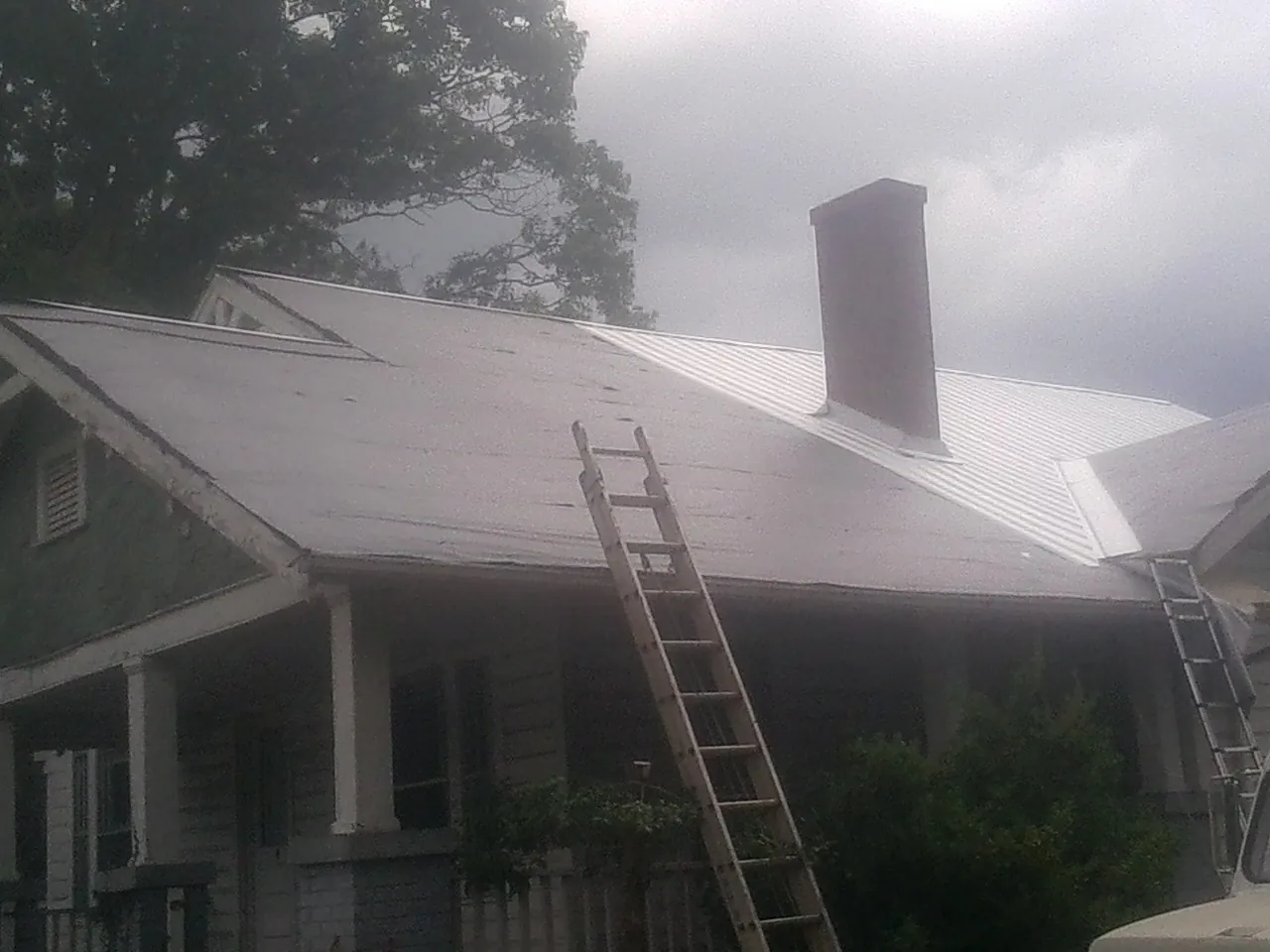 Ladders against a metal roof on an older home with a brick chimney in Liverpool