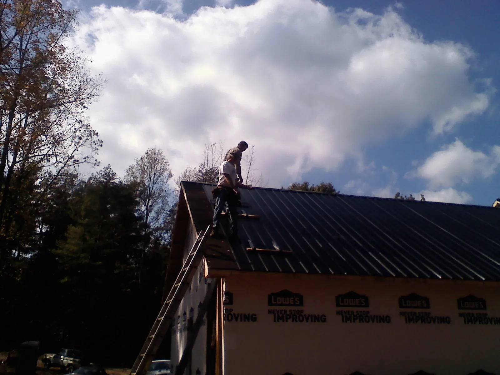 Roofer fastening dark metal panels high against a cloudy sky, from a Roof Inspection job in Liverpool